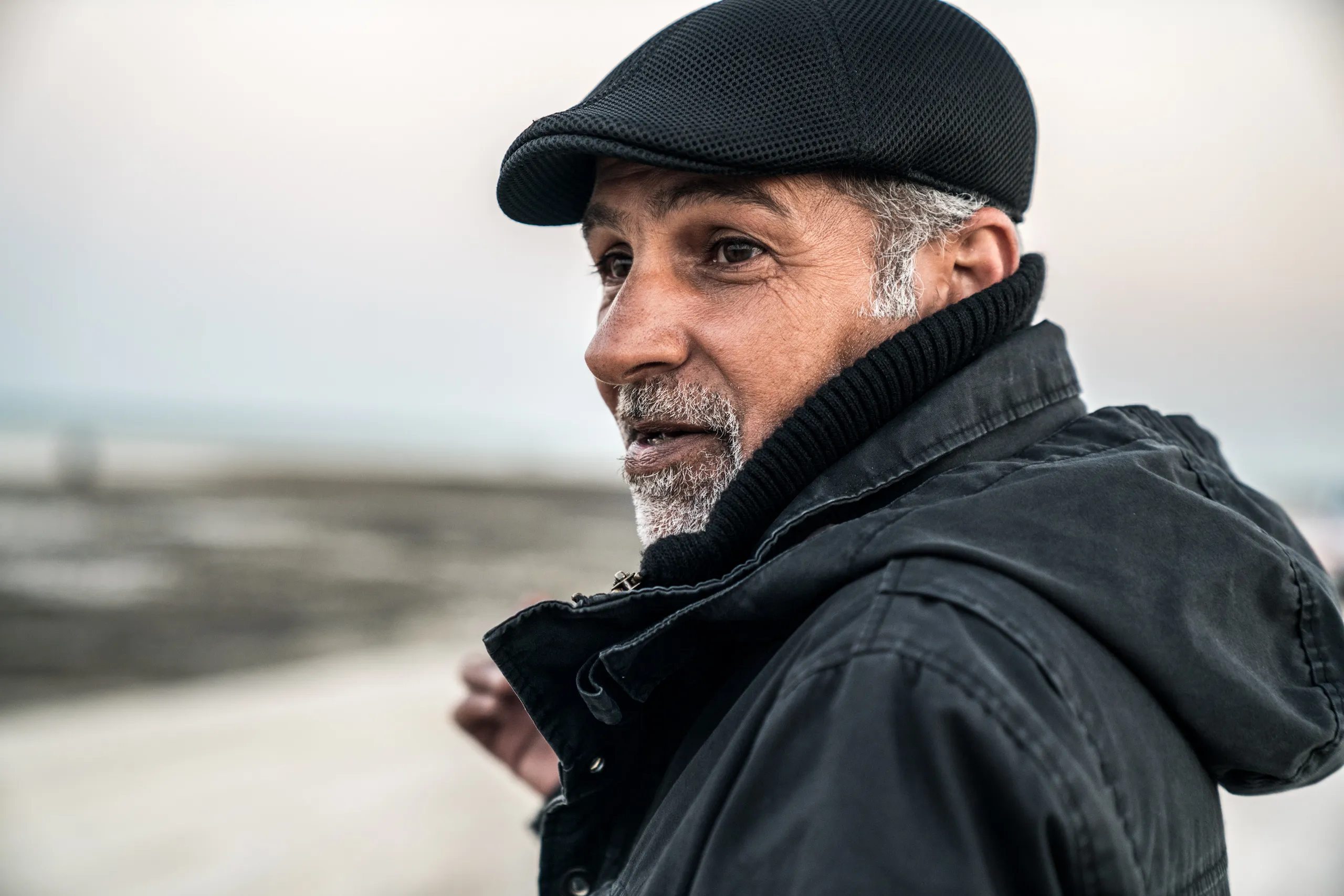 A man in a flat cap on the shore