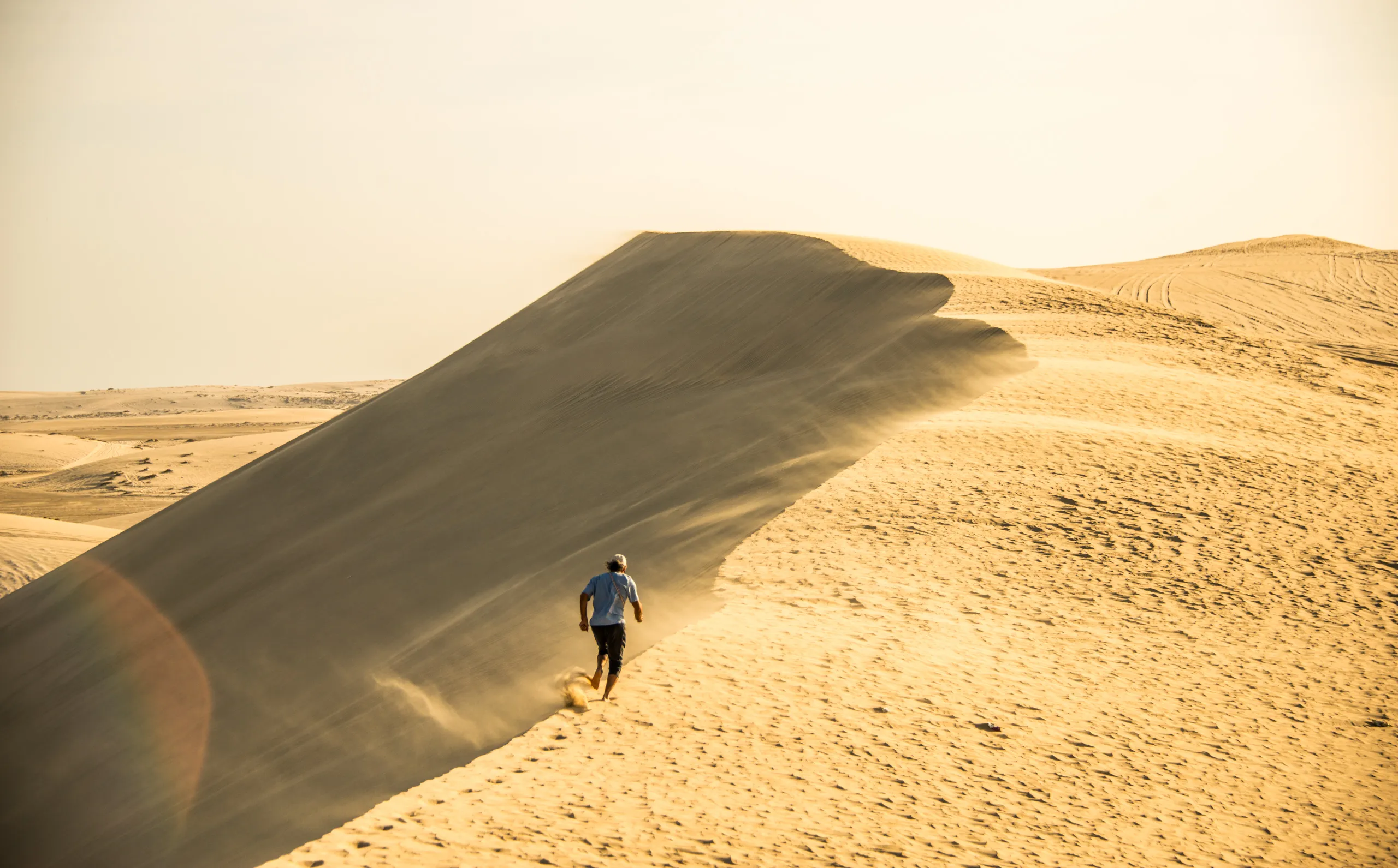 A man walking up the ridge of a dune